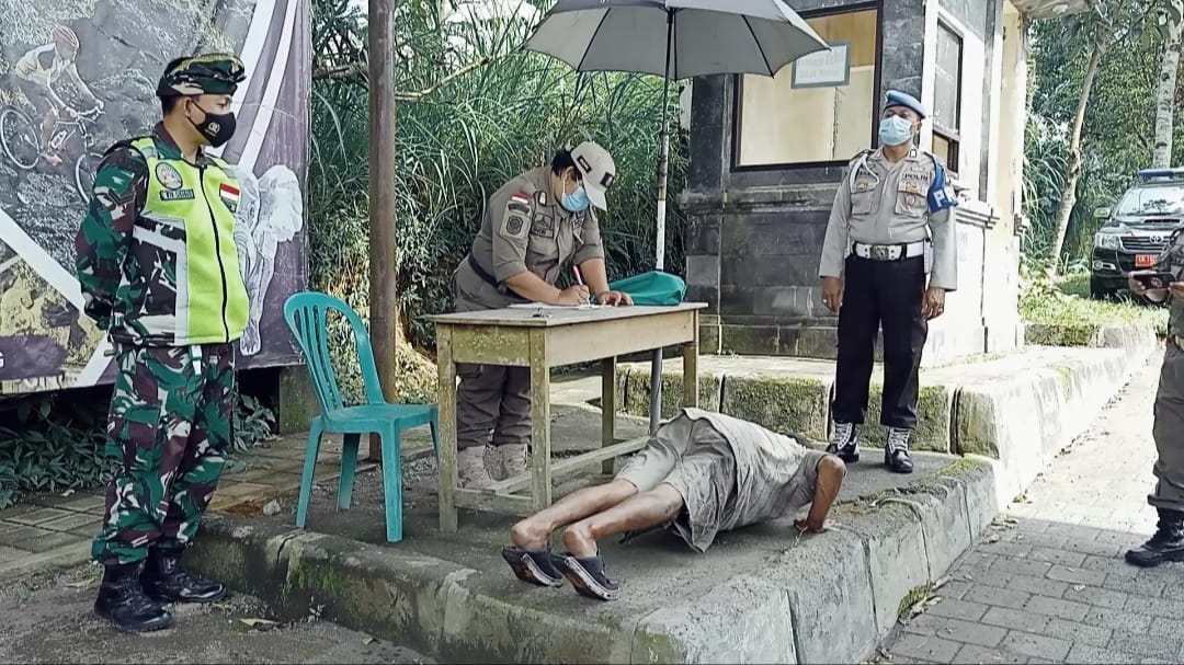 Seorang wisatawan yang tidak memakai masker dihukum push up oleh tim yustisi saat operasi di kawasan wisata Kintamani. Foto: Lintasnusanews.com/Ist